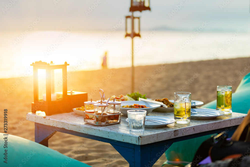 Food and beverage on the table at beach bar for dinning party on the beach and have sunset light and blurry sea background.