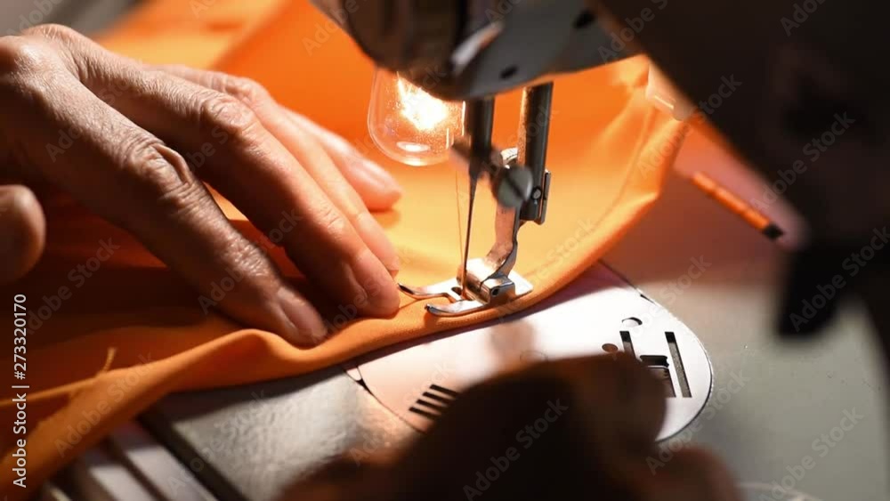 Woman sewing, Hands of old woman sewing dress from orange silk material on old vintage sewing machine close up