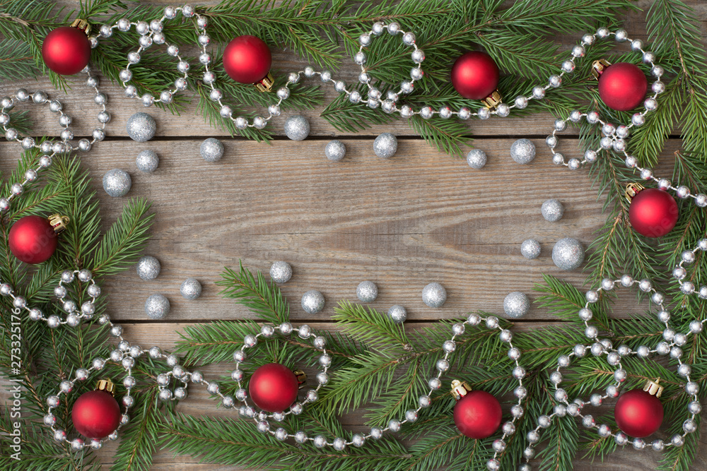 Christmas card concept with fir tree branches, red baubles, brocade globules and silver bead chain wooden background, deep side shadows - text space