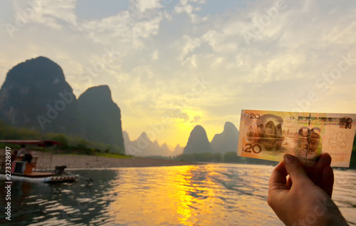 The tourist holds in her hand a bill of 20 yuan which depicts this place on the Li (Lijiang) River with green karst hills. Unusual natural park. Tourism in beautiful places in China