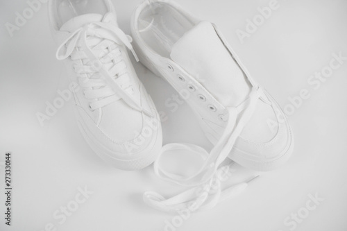 New white female or teen textile sneakers isolated on white background. White rubber-sneakers with untied laces on a light gray background. Use for banners, promotional flyers