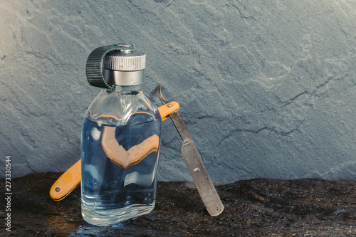 Clear blue aftershave bottle with old razor on wet stone texture photo