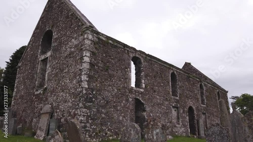 The gable end of a church ruin, with headstones in the churchyard cemetery. Panning left. photo