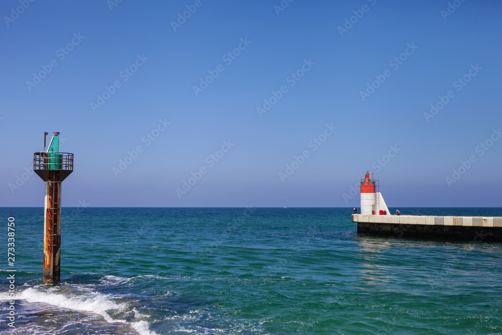 A lighthouse in the sea. White concrete dock in the ocean. Summer at France