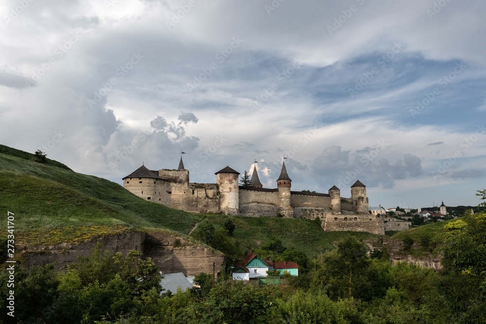 Landscape is the Kamianets-Podilskyi fortress of the XVI century, located far away on a green hill, under a beautiful cloudy sky. Ukraine.