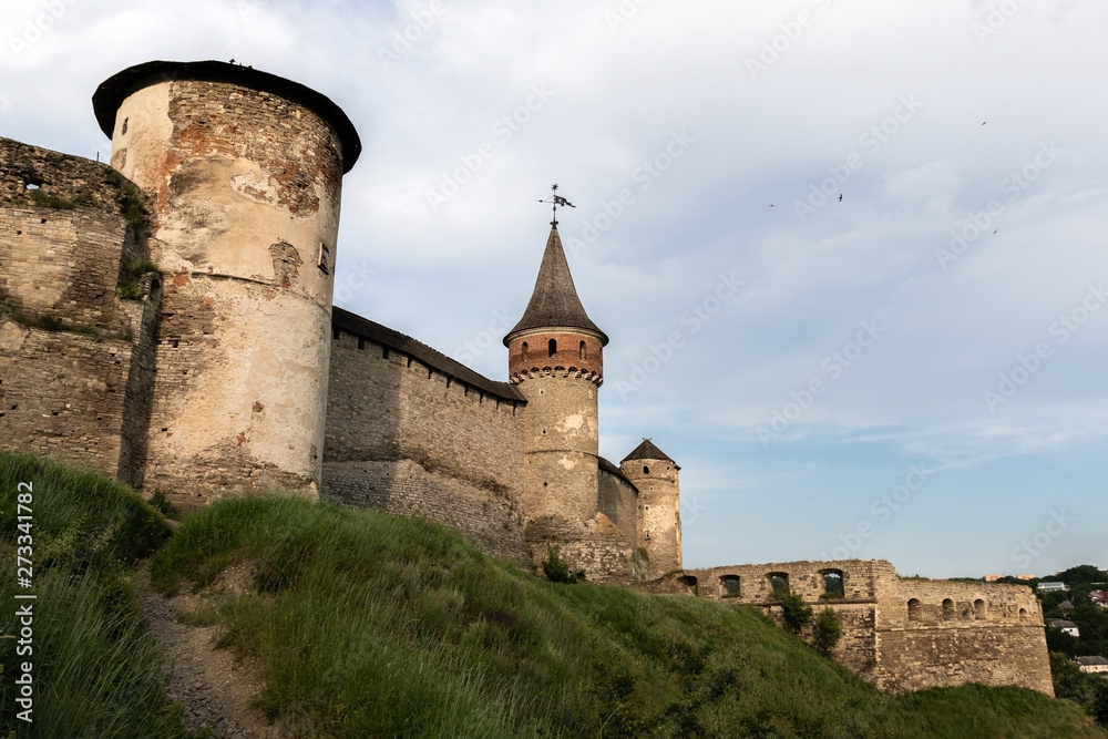 Three towers and stone walls of the medieval fortress of the XVI century in the city of Kamianets-Podilskyi on the background of blue sky with birds. Ukraine.