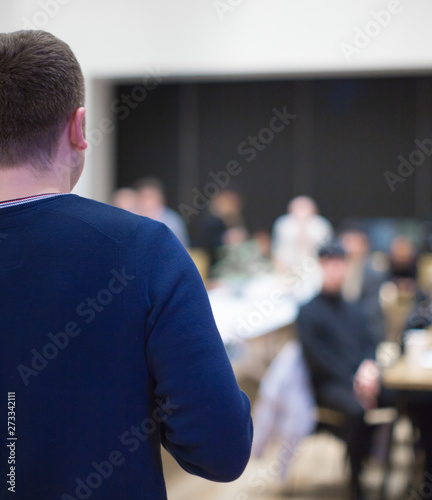 "Speaker giving a talk at a business conference. Audience in hall with presenter giving presentation. Tech executive giving speech during business and entrepreneur seminar."