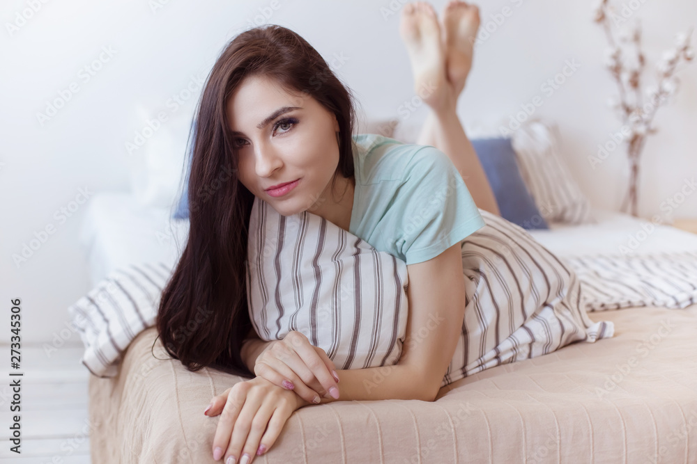 Beautiful brunette woman lies in bedroom on bed, and looks at frame. Life style Beautiful brunette woman lies in bedroom on bed, and looks at frame. Life style