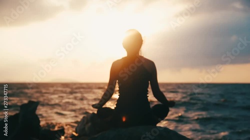 Young woman in bodysuit practicing yoga on the beach above sea at amazing sunrise.