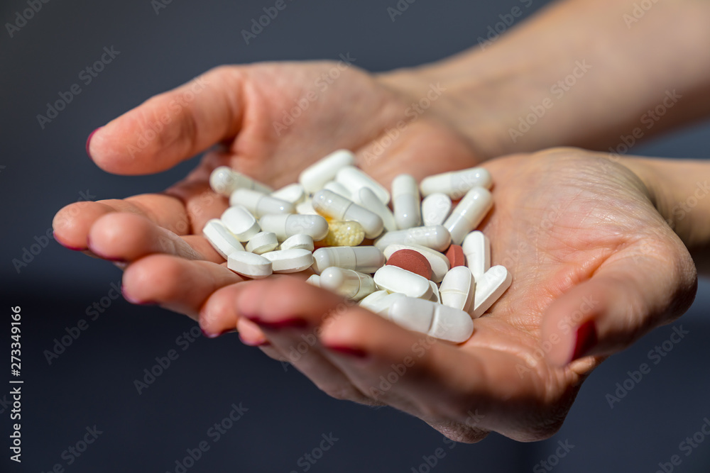 Both hands of a female girl with red fingernails holding many colorful pills and tablets as medicine and supplement for good health on grey background Both hands of a female girl with red fingernails holding many colorful pills and tablets as medicine and supplement for good health on grey background