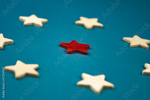 a bunch of wooden stars and one of them is highlighted in red. subject on blue background.