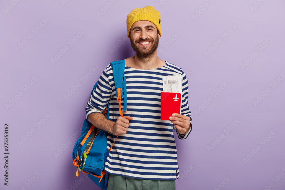 Indoor shot of optimistic tourist holds passport and tickets, carries rucksack, waits for flight, ready for vacation, enjoys travel, receives visa for traveling abroad, dressed in casual outfit Indoor shot of optimistic tourist holds passport and tickets, carries rucksack, waits for flight, ready for vacation, enjoys travel, receives visa for traveling abroad, dressed in casual outfit