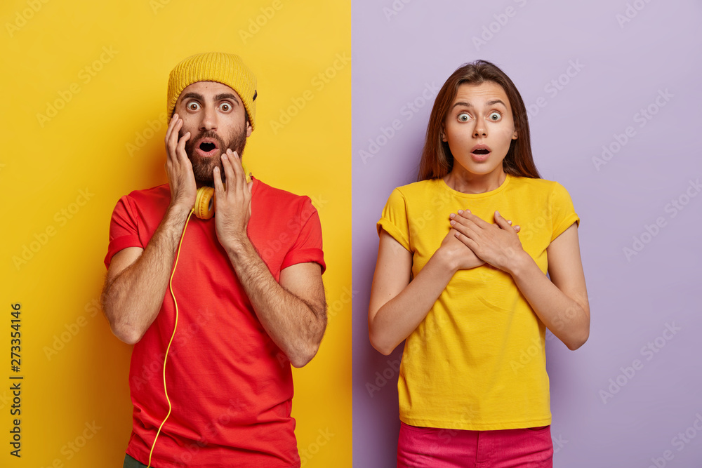 Omg concept. Stupefied young woman and man have bated breath, being speechless from fear, have shocked facial expressions, gaze at something scarying, pose over purple and yellow vertical stripes Omg concept. Stupefied young woman and man have bated breath, being speechless from fear, have shocked facial expressions, gaze at something scarying, pose over purple and yellow vertical stripes