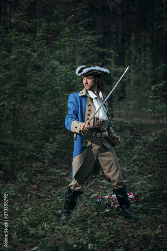 Man dressed as soldier of War of Independence USA attacks with saber in battle. 4 july independence day of USA concept photo composition: soldier, pistol, saber and flag.