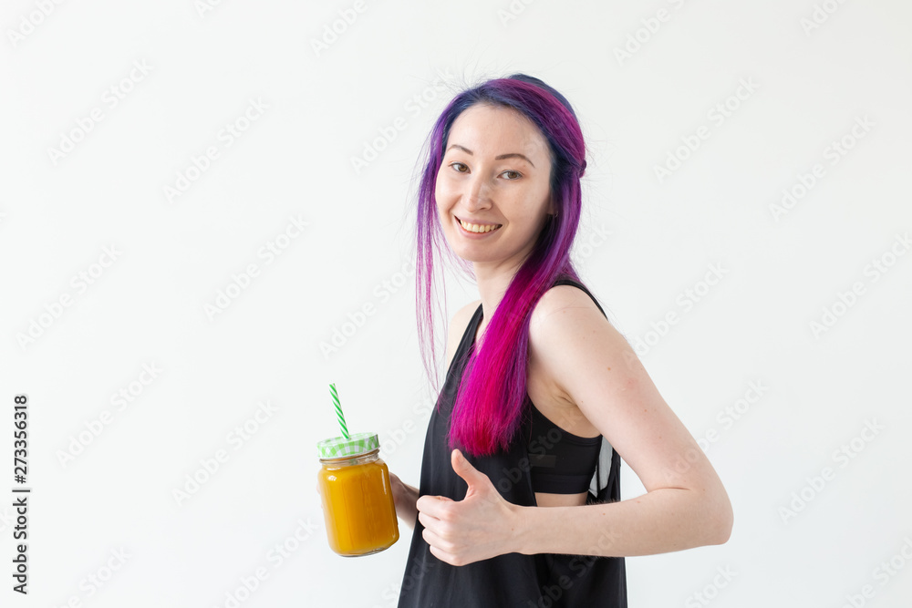 Portrait of a positive young mixed race and hipster girl with colored hair drinking fruit protein smoothie and showing thumbs up on a white background with copy space. Healthy lifestyle concept Portrait of a positive young mixed race and hipster girl with colored hair drinking fruit protein smoothie and showing thumbs up on a white background with copy space. Healthy lifestyle concept