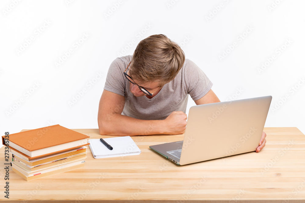 People and education concept - Funny student man sitting at the wooden table with laptop and books People and education concept - Funny student man sitting at the wooden table with laptop and books