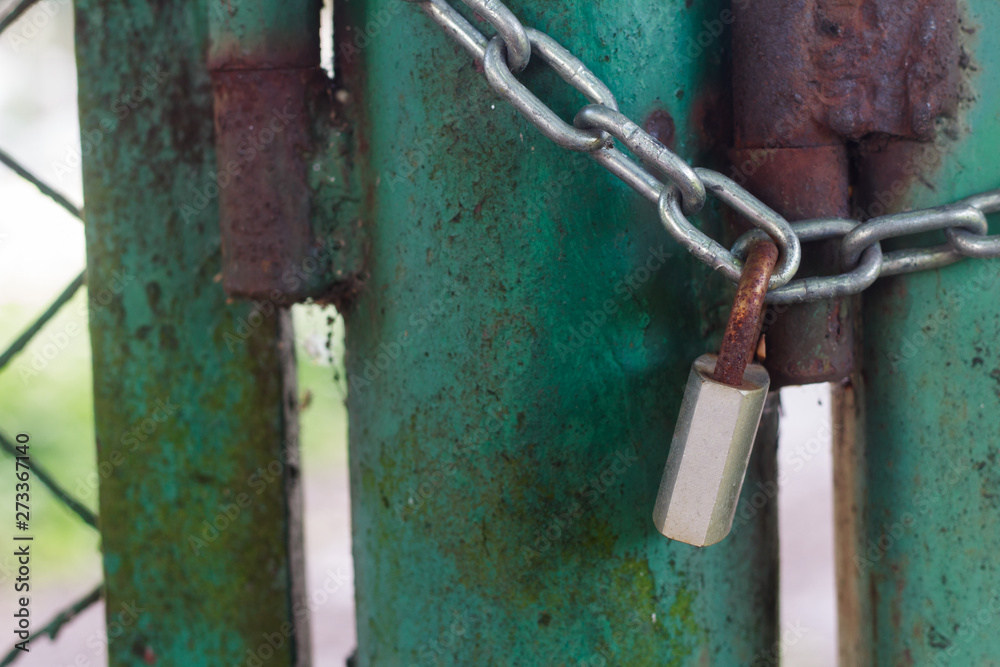 Closed green old gate with a rusty padlock and metal chain Closed green old gate with a rusty padlock and metal chain
