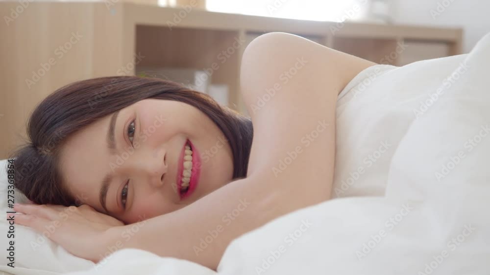 Asian woman smiling lying on bed in bedroom, Beautiful japanese female using relax time after wake up at home. Lifestyle women using relax time at home concept. Slow motion shot. Asian woman smiling lying on bed in bedroom, Beautiful japanese female using relax time after wake up at home. Lifestyle women using relax time at home concept. Slow motion shot.