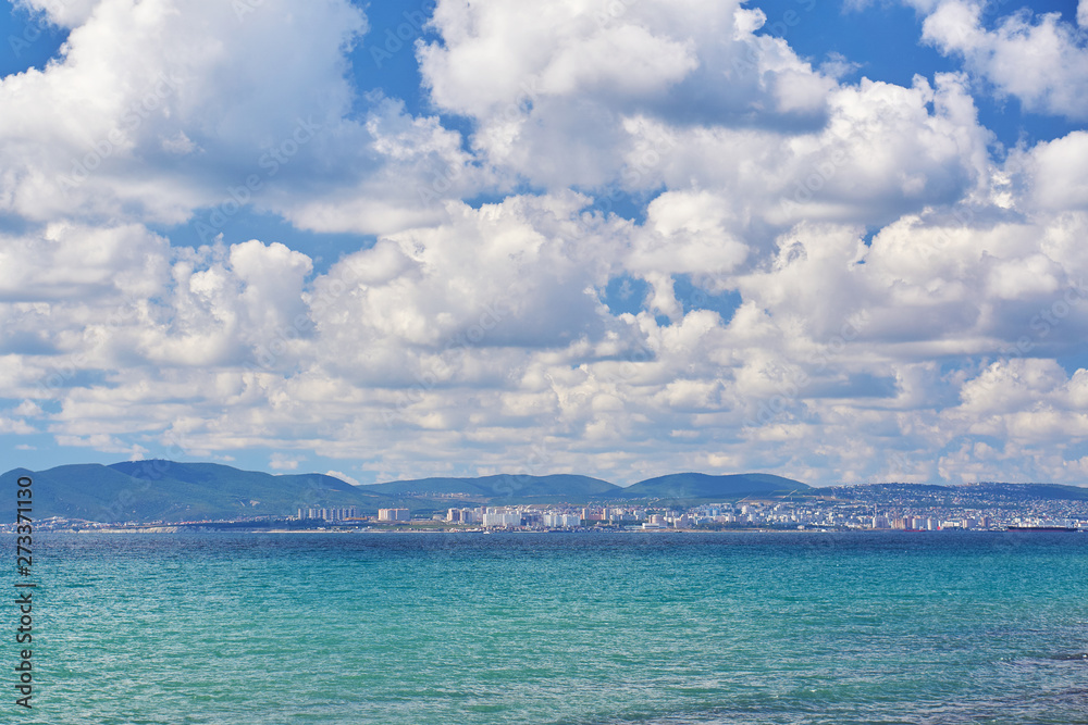 Pearl waves of the sea resort to the shore against the background of mountains, city and clouds Pearl waves of the sea resort to the shore against the background of mountains, city and clouds