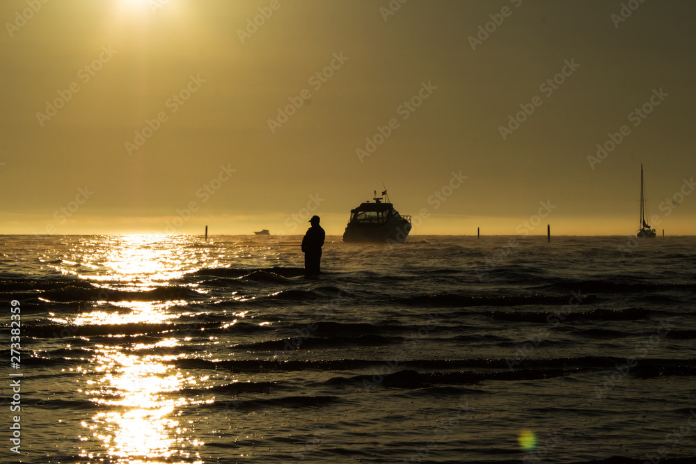 silhouette of a fisherman with a fishing rod and boats in the sea