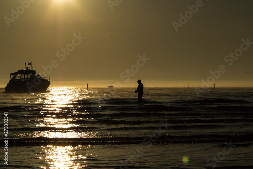 silhouette of a fisherman with a fishing rod and boats in the sea