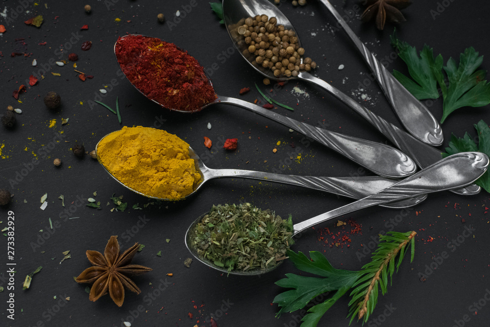 Set of various spices and herbs on black slate background. Pepper, turmelic, ginger, saffron, basil, rosemary, chilly, cardamom, cinnamon, anise. Top view with copy space.