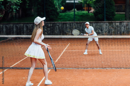 Two fit woman in cap and tennis uniform serving tennis ball during training on the outdoor tennis court. © Тарас Нагирняк