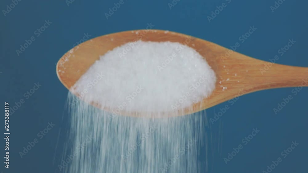 macro video shooting ,wooden spoon pouring sugar isolated on a blue background , concept of cooking sweet sugar addiction unhealthy diet overweight and obesity 