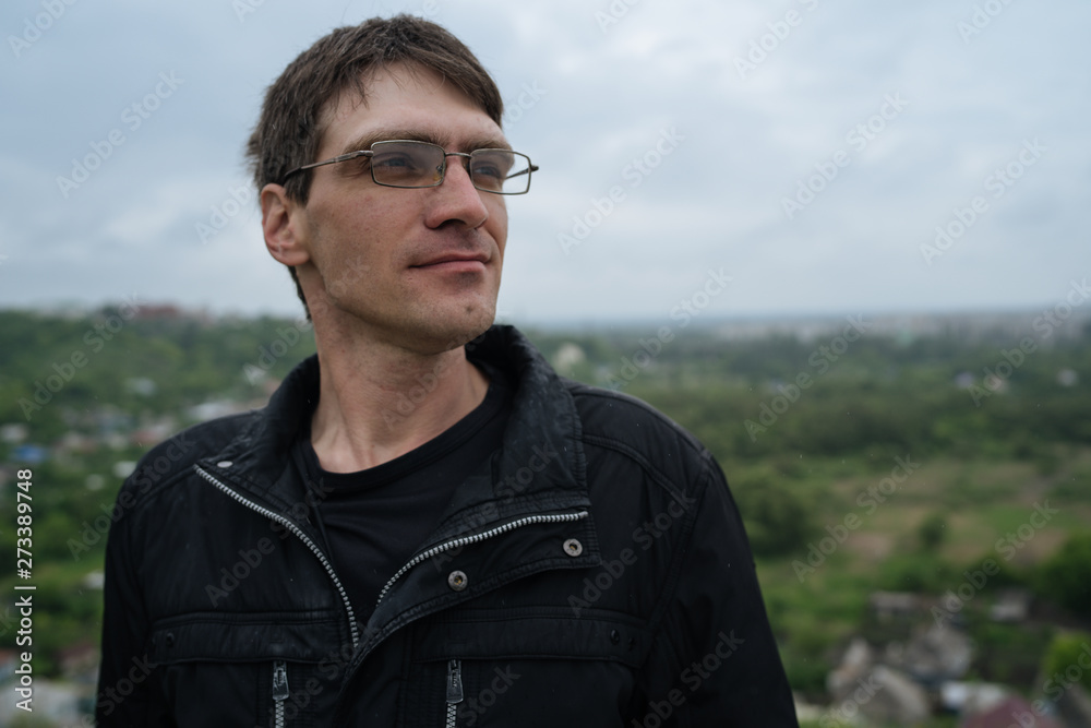 The man in glasses looks thoughtfully into the distance, standing on the street in the summer. Street style clothing The man in glasses looks thoughtfully into the distance, standing on the street in the summer. Street style clothing