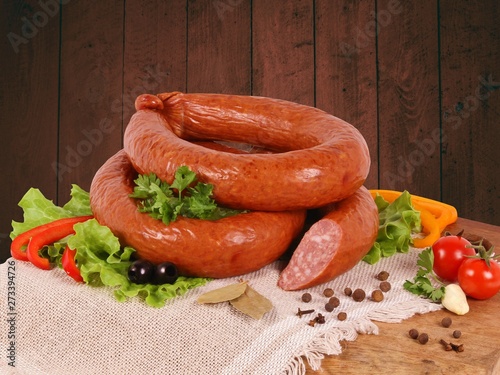 Smoked sausage with vegetables, herbs and spices on a wooden Board on a wooden background.