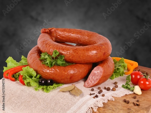 Smoked sausage with vegetables, herbs and spices on a wooden Board on a dark background.