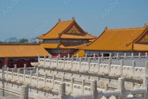 Orange roofs of traditional chinese buildings with white marble pillars in foreground