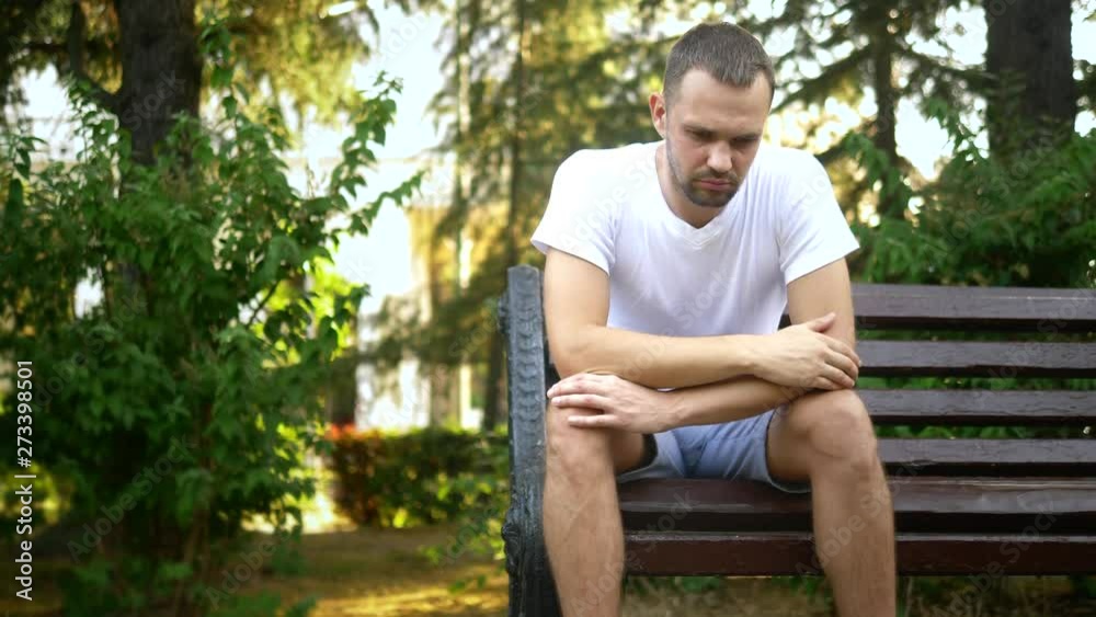 Depressed Sad young man sitting alone on a bench in a summer park. copy space Depressed Sad young man sitting alone on a bench in a summer park. copy space