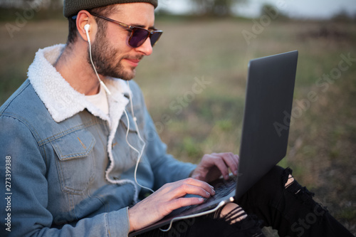 Smiling guy working on laptop with earphones in the meadowlands  photo