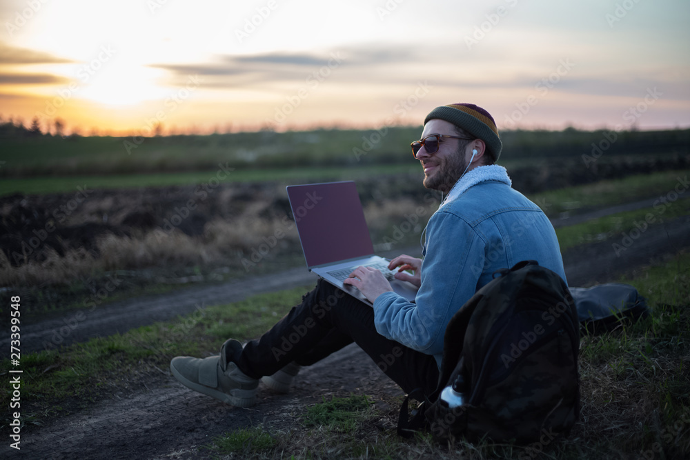 Smiling guy working on laptop with earphones on in the meadowlands 