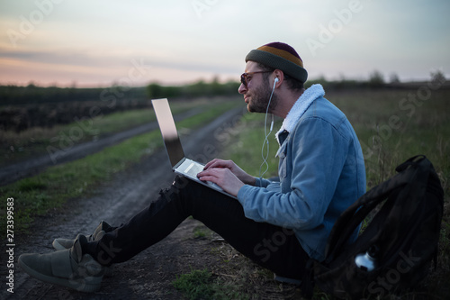 Smiling guy working on laptop with earphones on in the meadowlands  photo