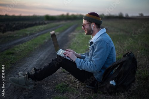 Smiling guy working on laptop with earphones on in the meadowlands  photo
