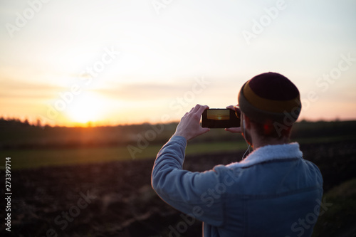 Back view of young guy take pictures of sunset by smartphone © Lalandrew