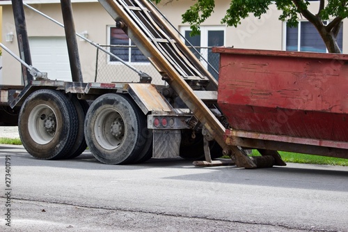 Empty roll-off construction dumpster being unloaded from truck at residential construction site