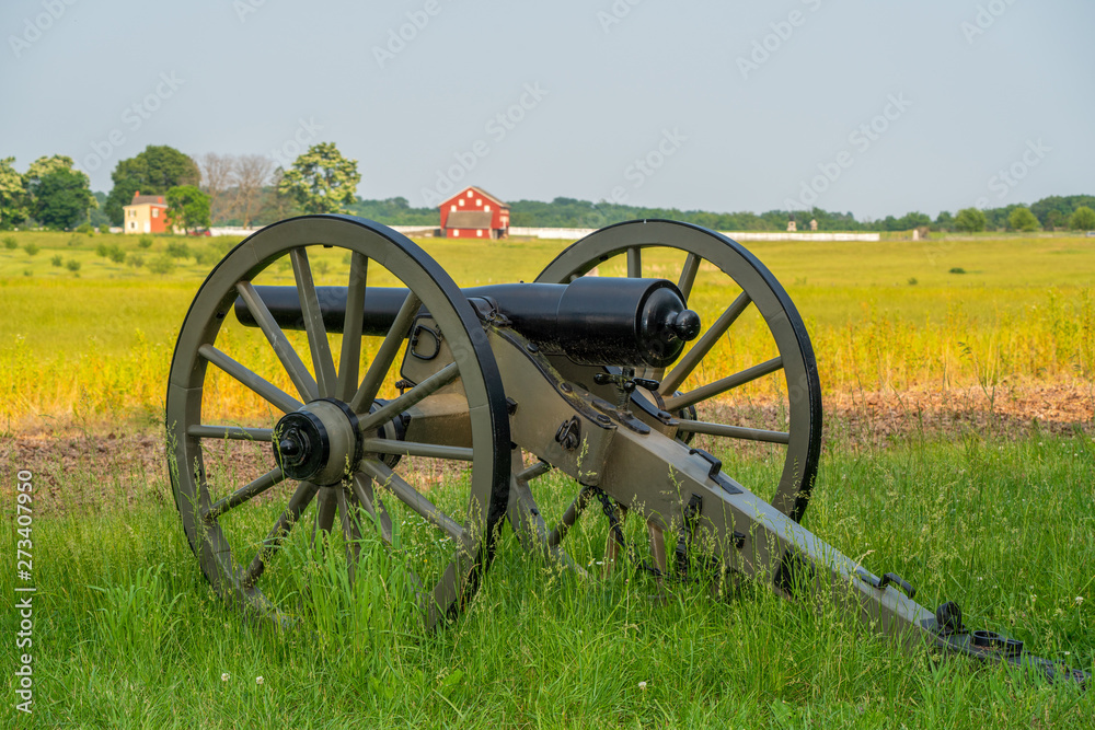 Civil war cannon seating in green grassy field with red barn in background on Gettysburg PA battlefield.
