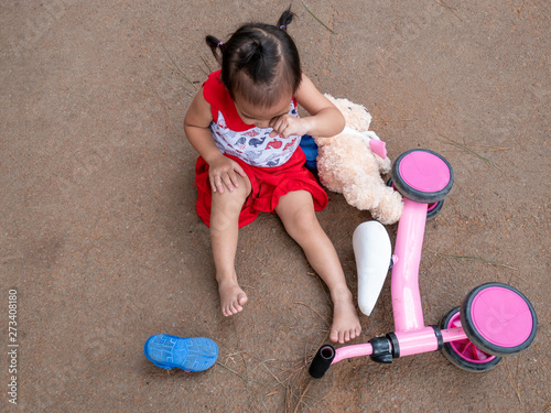Obraz na plátně Asian little girl sitting on the ground after falling and getting hurt at knee while riding a bicycle at summer park