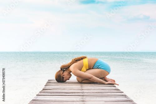 Vacation of Asian woman relaxing in yoga Child's Pose stretching exercises muscle for warm up on pier with beautiful beach and seaside in Thailand,so comfortable and relax in holiday,Healthy Concept