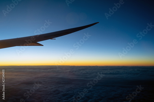 Scene of Airplane wing over the cloud and fantastic sky at sunrise time when flying above the land, Nature and travel concept