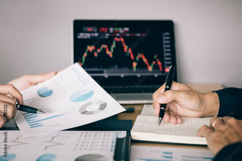 Two investors are working together with analyzing the stock data graphs in the paper and viewing the data on the laptop screen. Two investors are working together with analyzing the stock data graphs in the paper and viewing the data on the laptop screen.