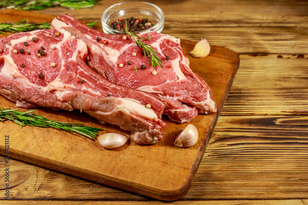 Raw fresh beef rib eye steak on bone with spices, garlic and rosemary on wooden table