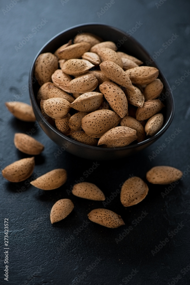Bowl of unpeeled almonds over black stone background, vertical shot, selective focus