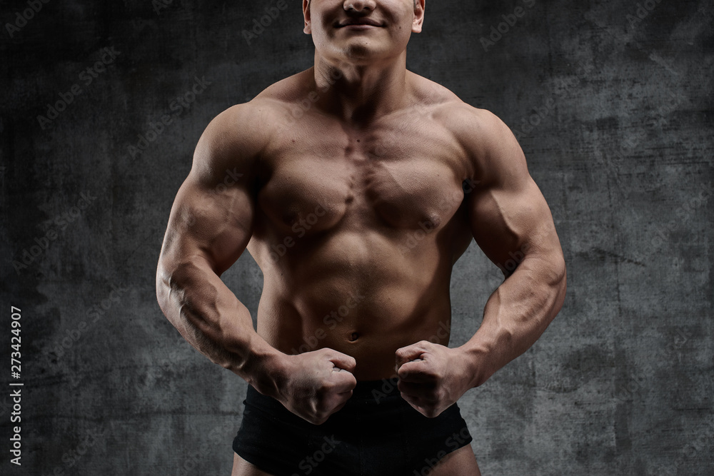 Sexy bodybuilder man posing on dark background in black shorts. Handsome pumped male body isolated with free space for advertising
