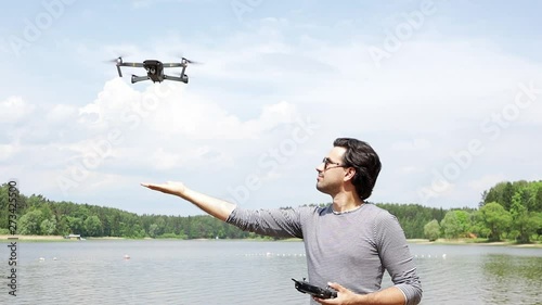 Young handsome man in sunglasses watching and navigating a flying drone with remote control, outdoor.   photo