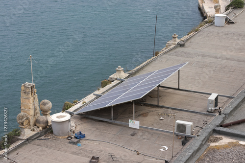 Solar panel on messy rooftop in mediterranean region next to body of water.
