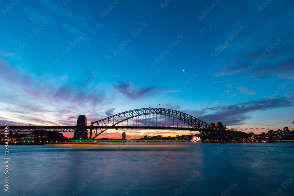 Naklejka premium Boat trail passing through Sydney Harbour Bridge at dusk.